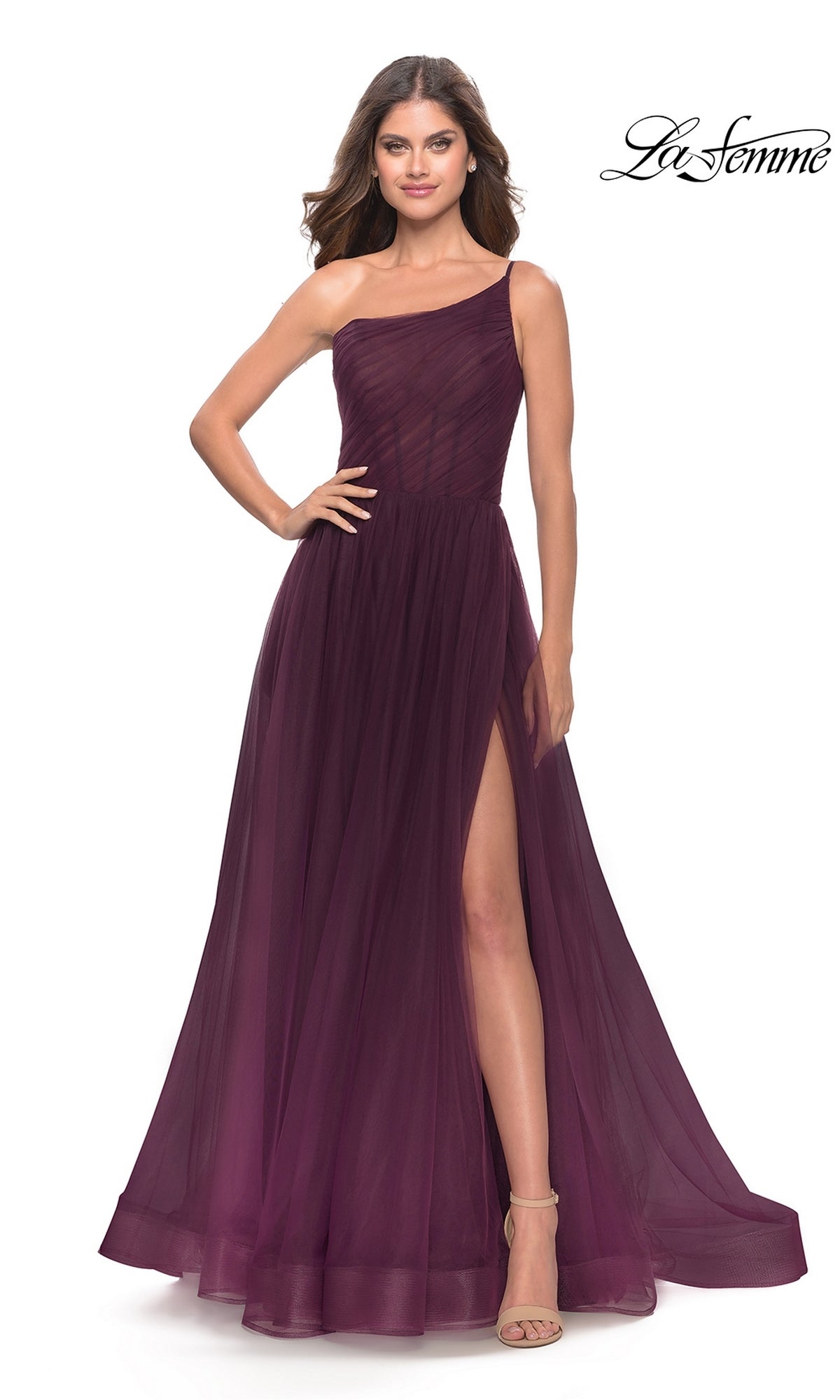 A woman wears the One-Shoulder Sheer-Bodice Prom Ball Gown 31069, a sleeveless, floor-length dark purple formal dress with a thigh-high slit, paired with beige high-heeled sandals. The La Femme logo appears in the top right corner.